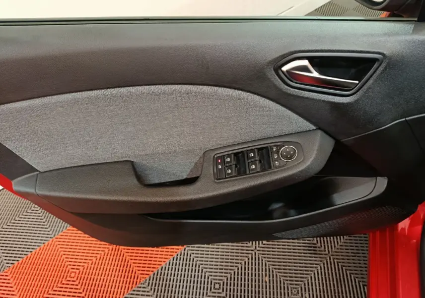 Vue intérieure côté conducteur de la porte d’une Renault Clio rouge 2024 avec commandes électriques et garniture tissu grise.