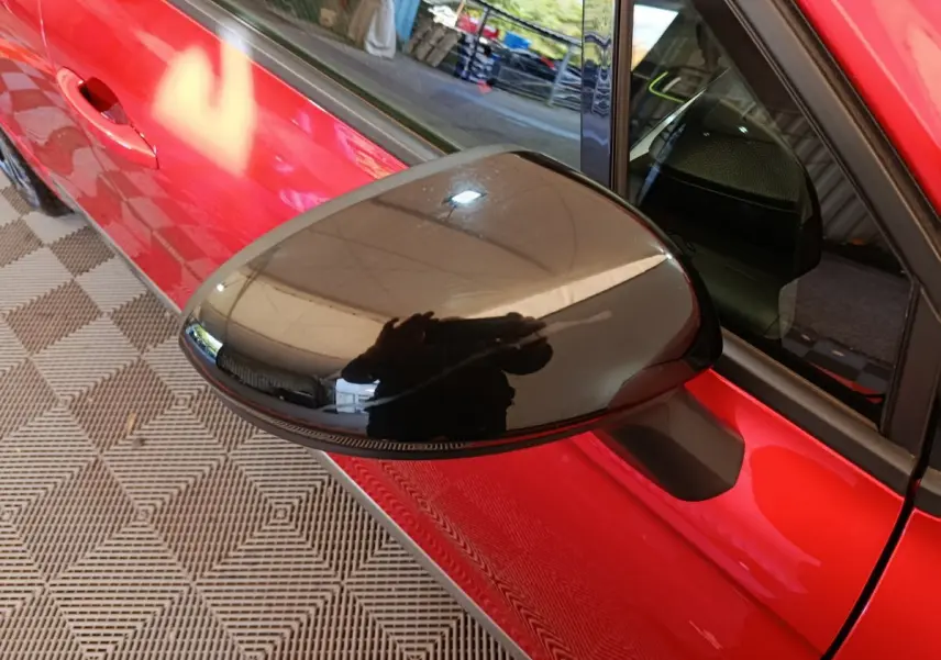 Rétroviseur noir en gros plan côté gauche d'une Renault Clio Techno TCe 90 rouge, vue partielle sur la porte.