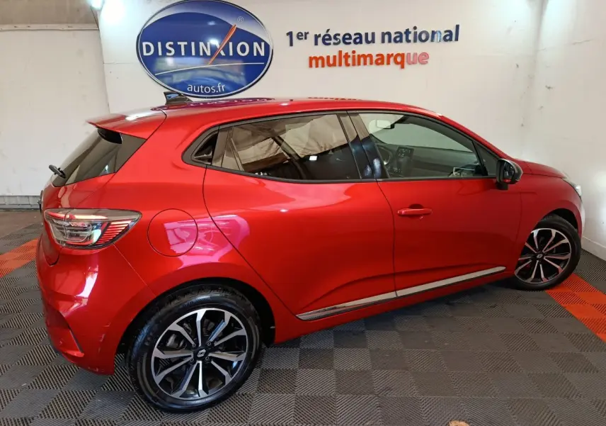 Vue latérale droite d'une Renault Clio Techno TCe 90 rouge 2024, avec jantes alliage et vitres teintées, en intérieur showroom.