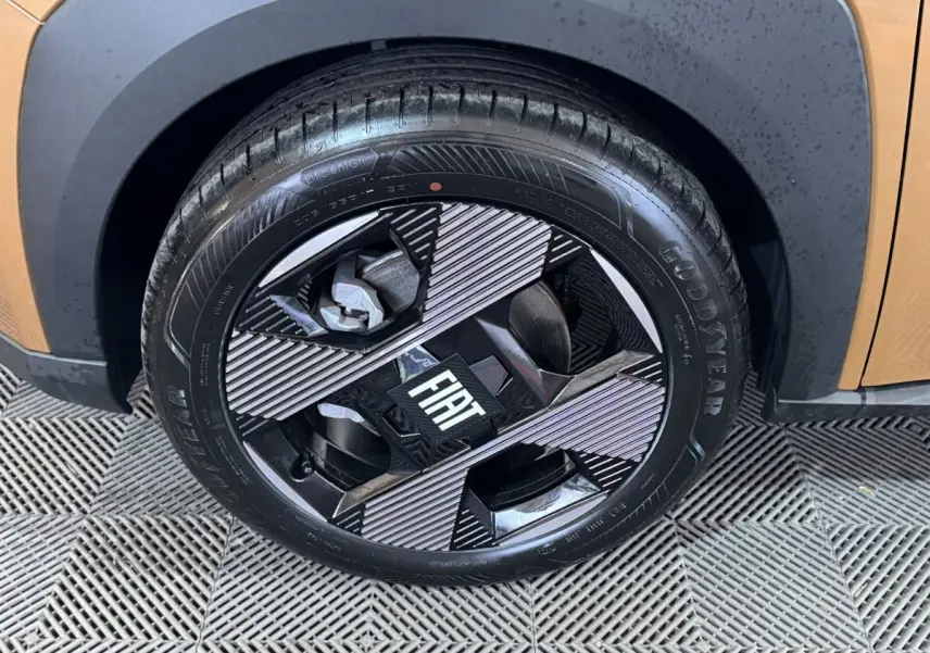 Gros plan sur la roue avant droite marron de la Fiat Grande Panda 1.2 Hybrid avec jante noire et argentée au design géométrique.