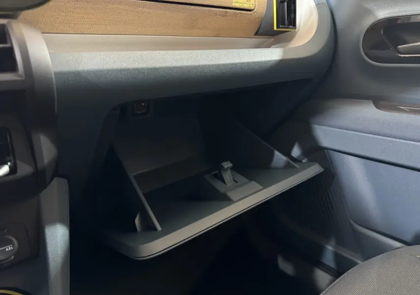 Gros plan sur la boîte à gants ouverte côté passager de la Fiat Grande Panda marron, intérieur sombre et moderne.