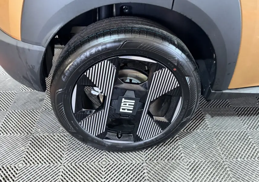 Gros plan sur la roue avant gauche marron de la Fiat Grande Panda 1.2 Hybrid avec jante noire et motifs rayés blancs.