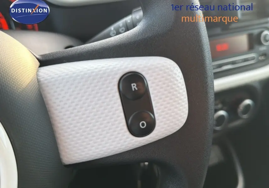 Gros plan sur le volant noir et blanc texturé de la Renault Twingo gris acier, avec boutons de commande visibles.