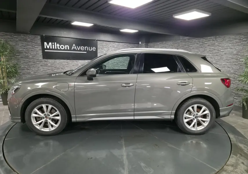 Audi Q3 gris en vue de profil côté gauche, avec jantes alliage et vitres arrière surteintées dans un showroom.