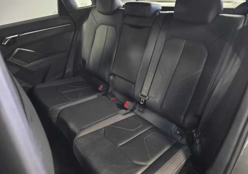 Vue intérieure montrant la banquette arrière en cuir noir de l'Audi Q3 S Line avec ceintures de sécurité et appuie-têtes.