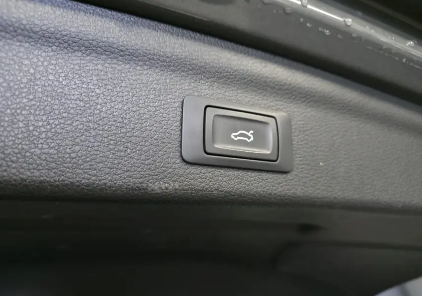Bouton d'ouverture électrique du hayon sur la garniture intérieure du coffre gris d'un Audi Q3 S Line hybride rechargeable.