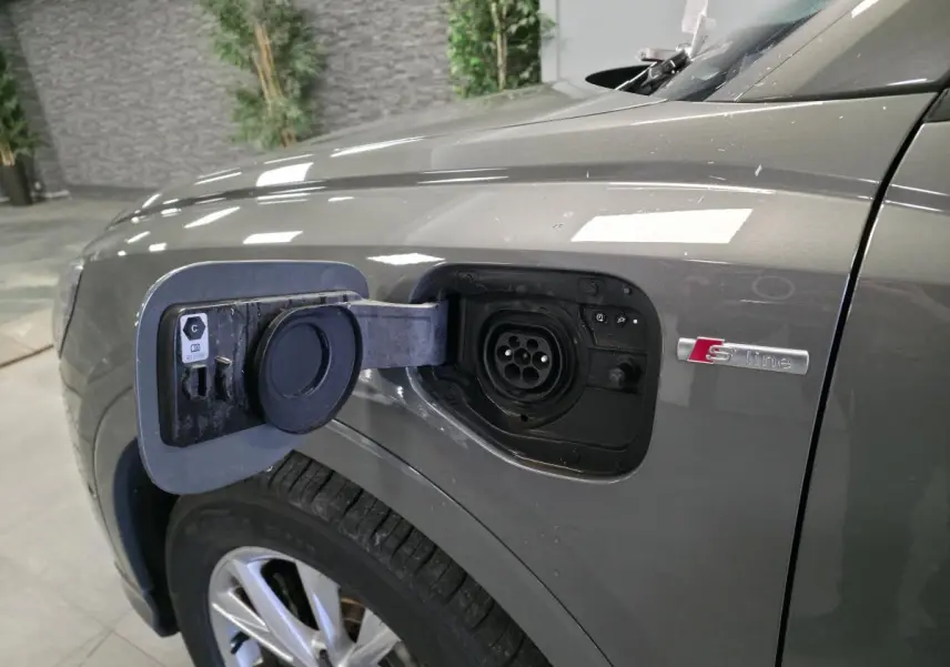 Prise de recharge ouverte sur le côté gauche d’un Audi Q3 gris S line, avec jante 5 branches visible.