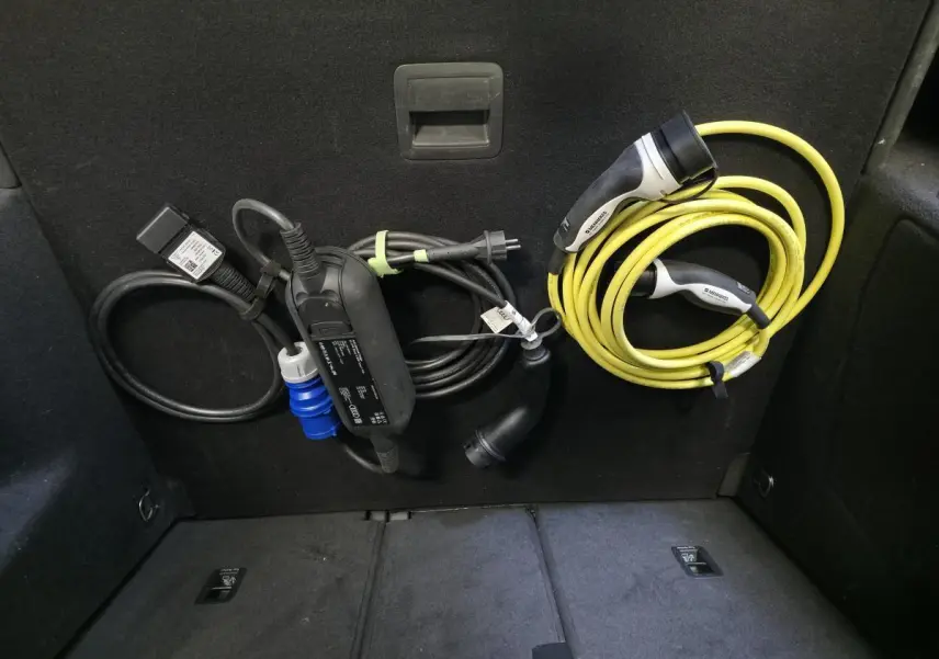 Coffre arrière d’Audi Q3 gris avec câbles de recharge hybride bien rangés sur la paroi intérieure.