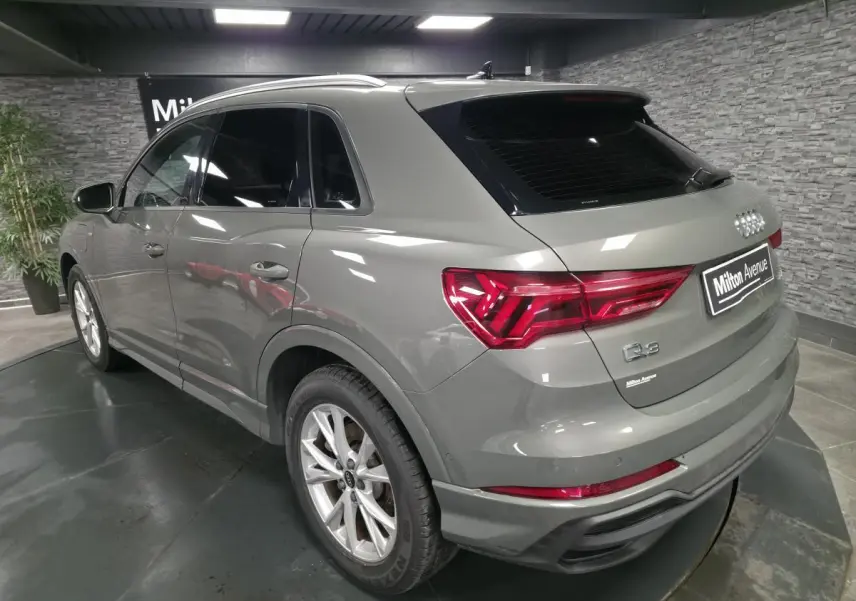 Audi Q3 gris métallisé en vue 3/4 arrière droit, avec vitres surteintées et feux arrière LED distinctifs.