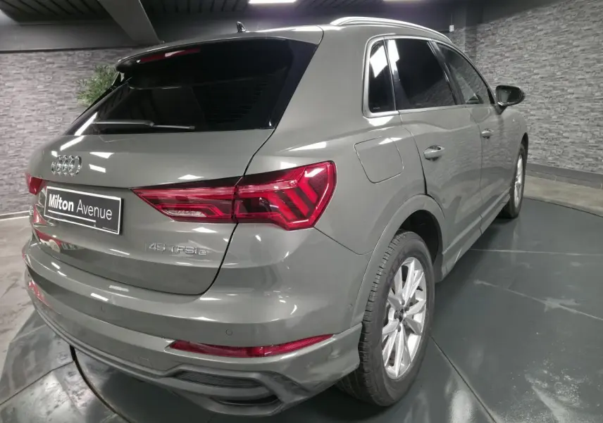 Audi Q3 gris en 3/4 arrière droit, avec vitres surteintées et feux arrière LED distinctifs.