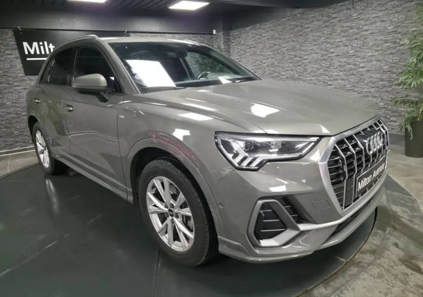 Audi Q3 gris en 3/4 avant droit, avec calandre large et phares LED distinctifs, stationné en intérieur showroom.