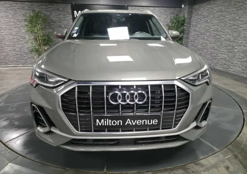 Vue avant d'un Audi Q3 gris métallisé avec calandre noire et phares Matrix LED dans un showroom.