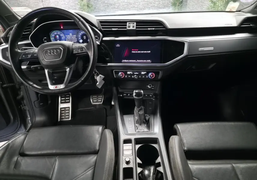 Vue intérieure avant de l'Audi Q3 gris, avec volant sport, tableau de bord numérique et console centrale moderne.