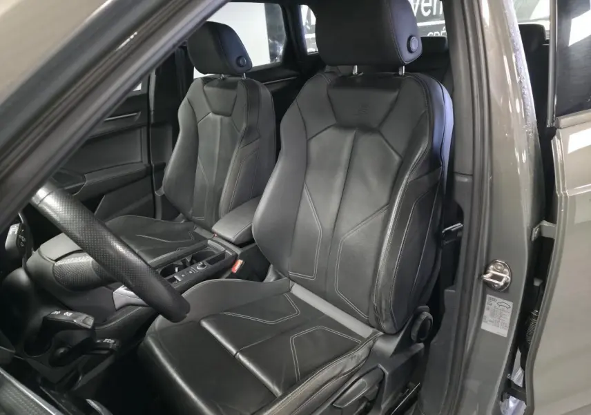 Vue intérieure côté conducteur de l'Audi Q3 gris, mettant en valeur les sièges sport en cuir noir avec surpiqûres.