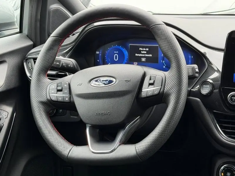 Vue rapprochée du volant sport noir avec surpiqûres rouges du Ford Puma 2024, affichage digital bleu du tableau de bord visible.