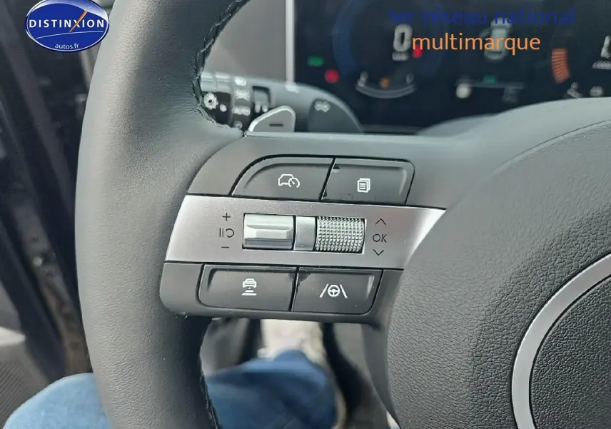 Gros plan sur les commandes au volant cuir du Hyundai Tucson noir abysse hybride 2025, avec tableau de bord numérique en arrière-plan.