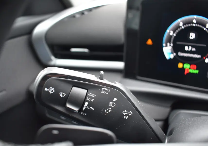 Gros plan sur la commande des essuie-glaces et clignotants dans l’habitacle du Volkswagen T-Roc blanc, tableau de bord numérique en arrière-plan.