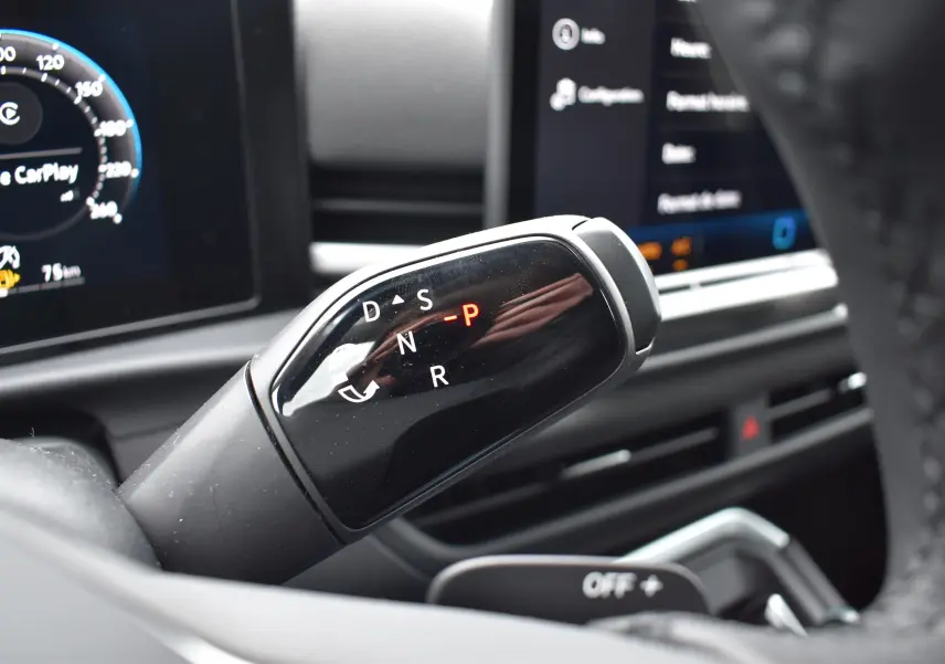 Gros plan sur le levier de vitesses automatique noir du Volkswagen T-Roc 2025, tableau de bord numérique en arrière-plan.