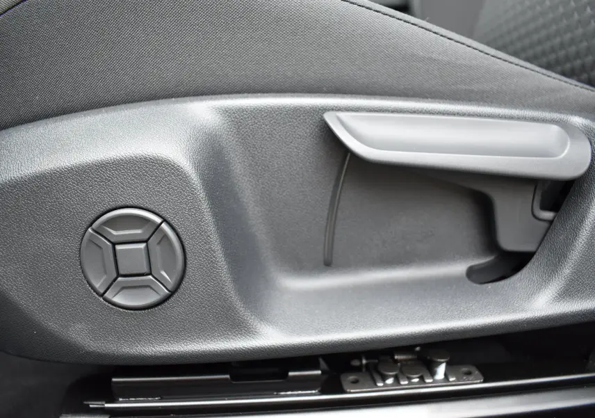 Gros plan sur la commande de réglage manuel du siège côté conducteur, plastique gris foncé.