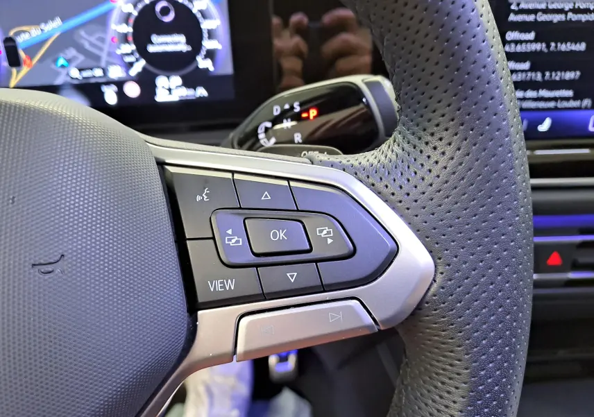 Gros plan sur les commandes multifonctions à gauche du volant perforé du Volkswagen Tiguan blanc 2025, version R-Line.