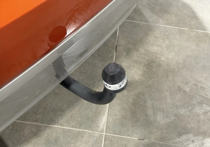 Gros plan sur l'attelage arrière noir d'un Suzuki Ignis orange 2022, vue partielle du pare-chocs gris.