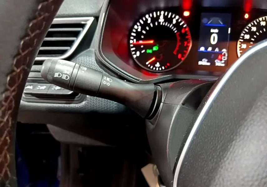 Gros plan sur le commodo des phares à gauche du volant cuir, avec tableau de bord éclairé en rouge de la Renault Clio Business.