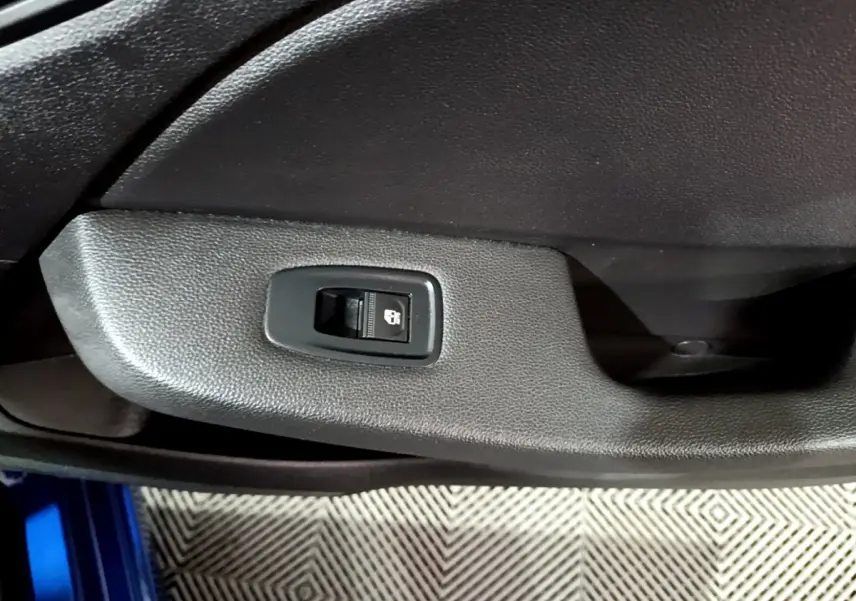 Gros plan sur le bouton de verrouillage centralisé sur la porte intérieure noire d'une Renault Clio bleu visible en bas.