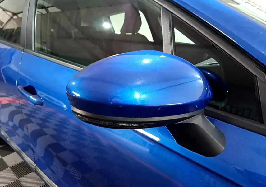 Gros plan sur le rétroviseur côté conducteur bleu métallisé d'une Renault Clio Business 2022, avec porte et vitre visibles.