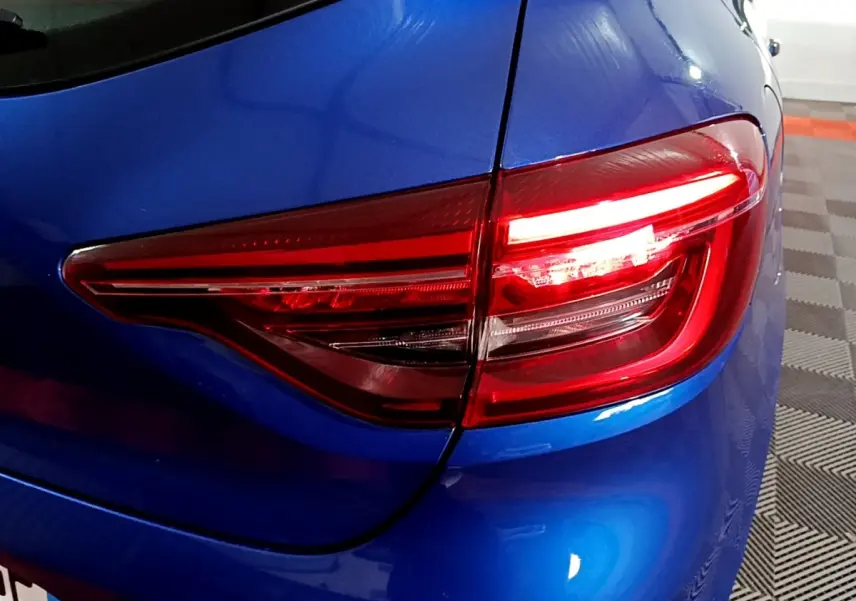 Gros plan sur le feu arrière droit rouge d'une Renault Clio Business bleu vif, avec carrosserie brillante et détails nets.