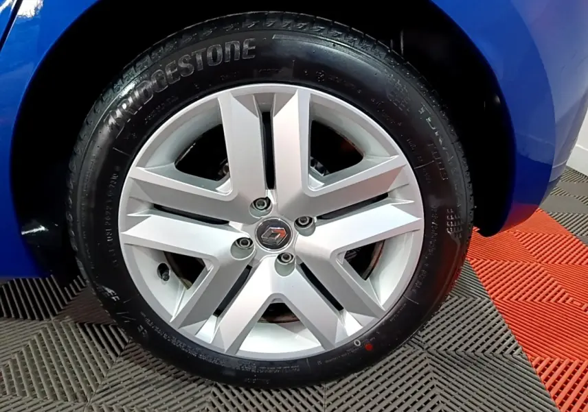 Vue rapprochée de la roue arrière droite d'une Renault Clio Business bleu vif sur sol à damier noir et rouge.