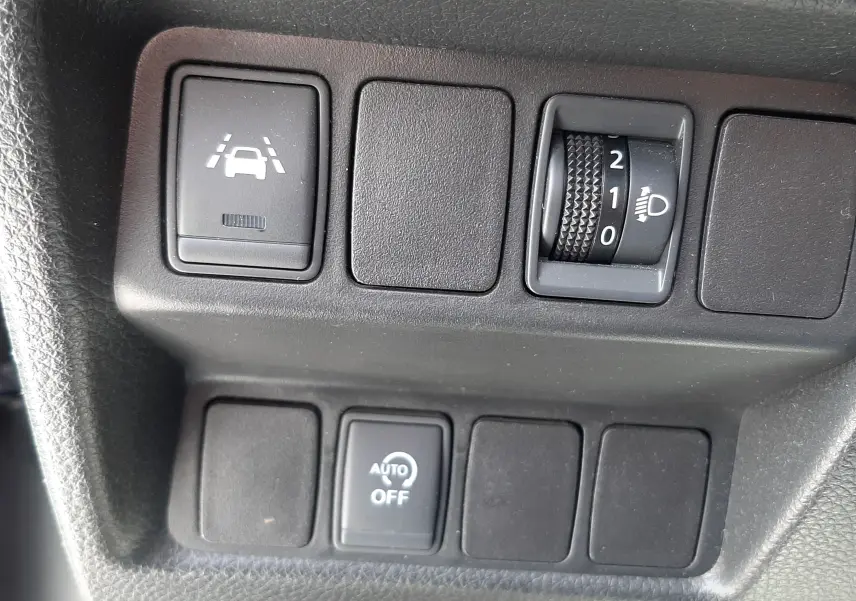 Gros plan sur les commandes intérieures noires du Nissan Qashqai 1.2 DIG-T 2018, avec réglage phares et assistance de maintien de voie.