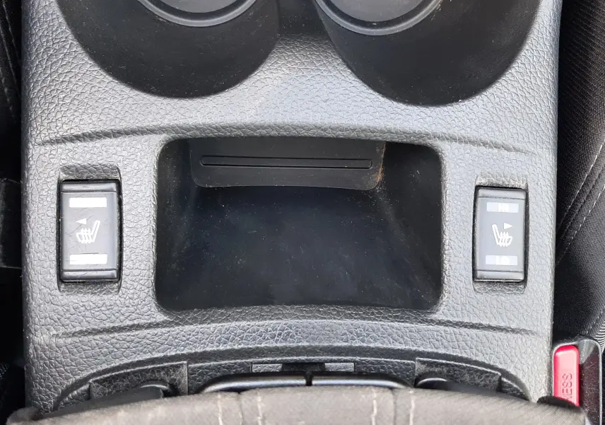 Vue rapprochée de la console centrale noire du Nissan Qashqai 2018 avec commandes de sièges chauffants et porte-gobelets.