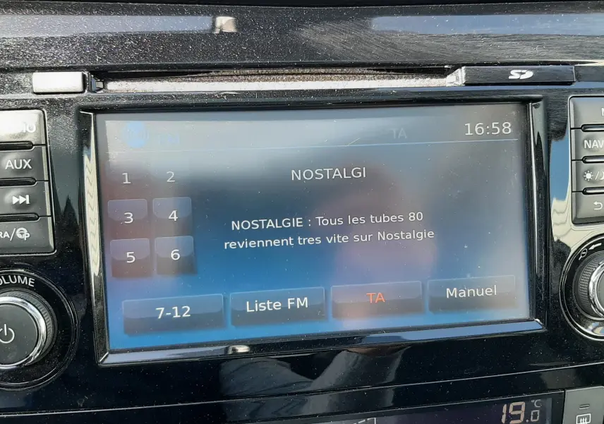 Gros plan sur l’écran multimédia et la console centrale d’un Nissan Qashqai marron métal, affichant la radio Nostalgie.