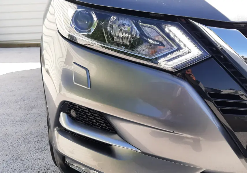 Gros plan sur l'avant droit du Nissan Qashqai marron métal, mettant en valeur le phare LED et la calandre chromée.