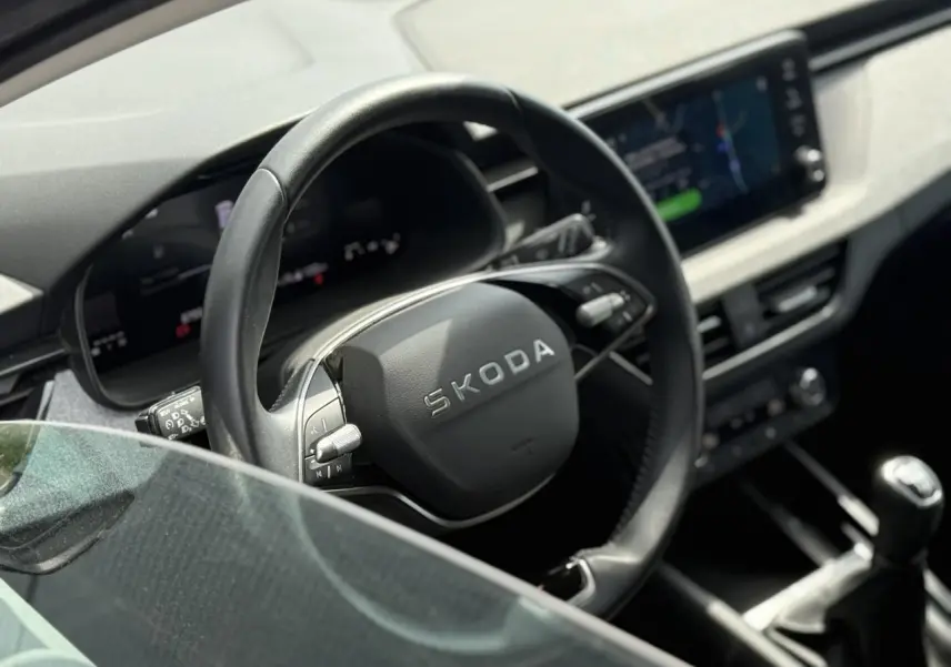 Vue intérieure rapprochée du volant en cuir noir et de la console centrale d’une Skoda Scala TSI 116 gris graphite.