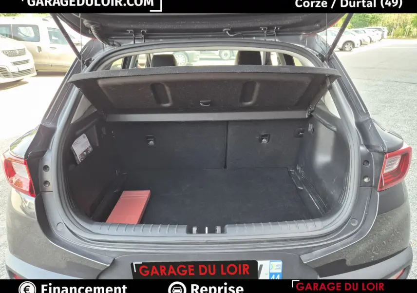 Coffre ouvert vue arrière d’une KIA STONIC 1.0 T-GDi 100 ACTIVE gris foncé avec cache-bagages relevé.