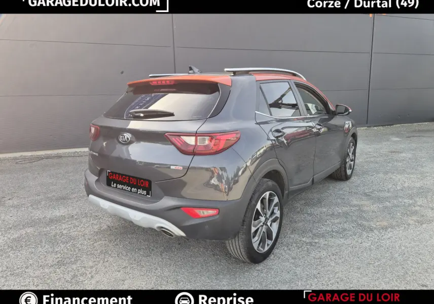 Vue 3/4 arrière droite d’un KIA Stonic 2019 gris foncé avec toit orange et barres de toit chromées.