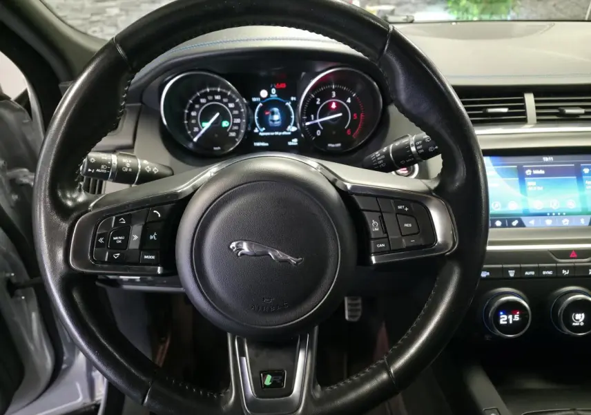 Vue centrée sur le volant cuir noir du Jaguar E-PACE gris, avec tableau de bord numérique et écran tactile visible à droite.