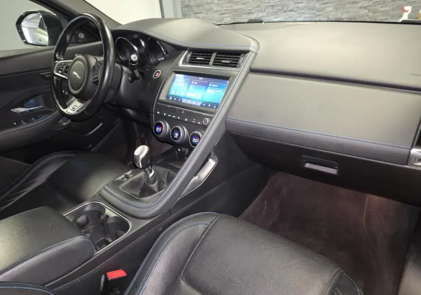 Intérieur Jaguar E-PACE D150 gris, vue côté passager avec console centrale et volant cuir multifonction.