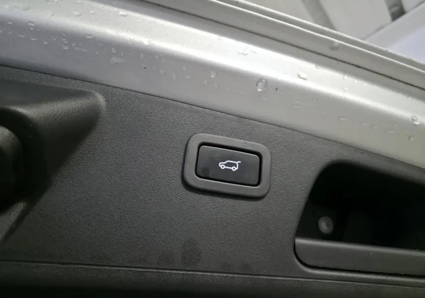 Bouton d'ouverture électrique du hayon sur la partie intérieure grise du coffre d'un Jaguar E-PACE gris.