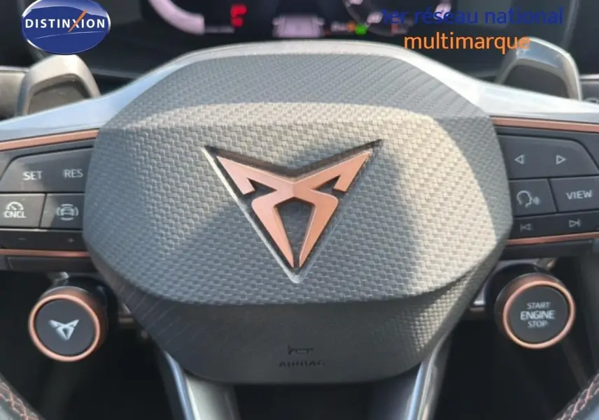 Gros plan sur le volant gris texturé avec logo CUPRA cuivré, boutons multifonctions et démarrage moteur visible.