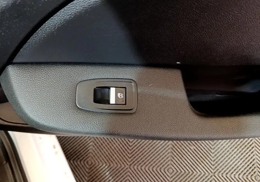 Gros plan sur le bouton de commande de la vitre électrique côté conducteur d’une Renault Clio blanche, intérieur noir.