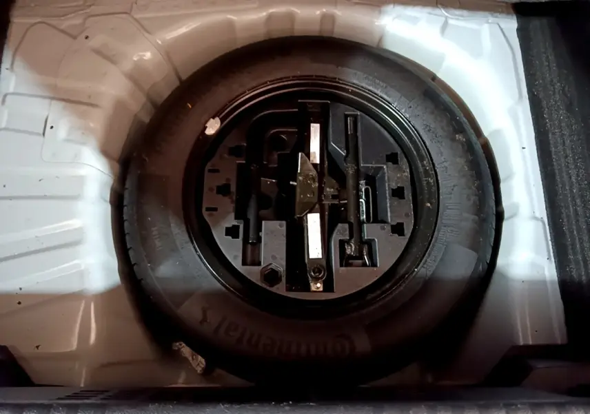 Vue plongeante sur la roue de secours noire et ses outils dans le coffre blanc d'une Renault Clio Business TCe 100 essence 2020.