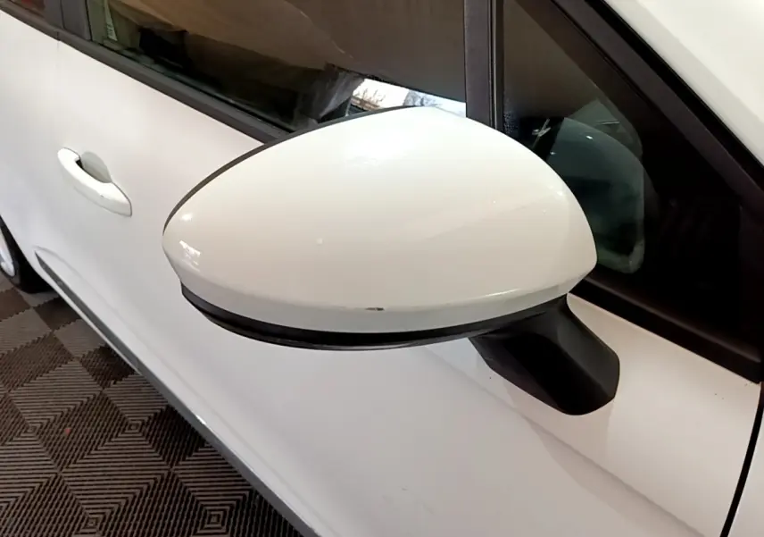 Gros plan sur le rétroviseur côté gauche blanc d'une Renault Clio Business TCe 100 de 2020, avec porte et vitre partiellement visibles.