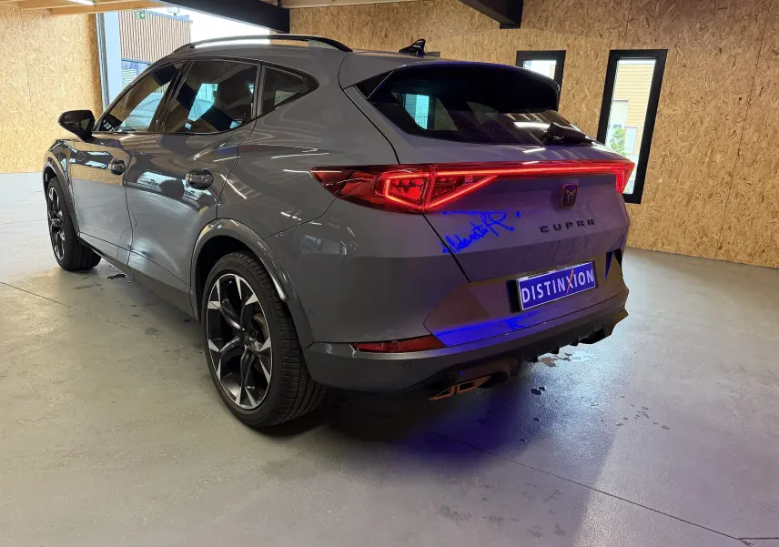 Vue 3/4 arrière droite du CUPRA Formentor gris 2023 avec feux arrière allumés et jantes noires distinctives.