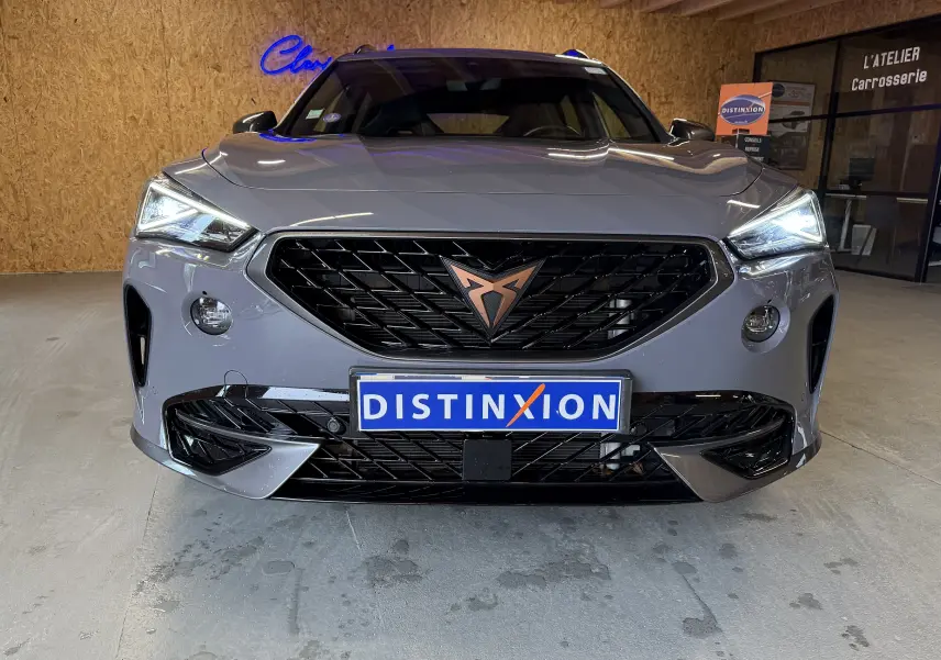 Vue frontale d'une CUPRA Formentor gris 2023 avec calandre noire et logo cuivré, phares LED allumés en intérieur.