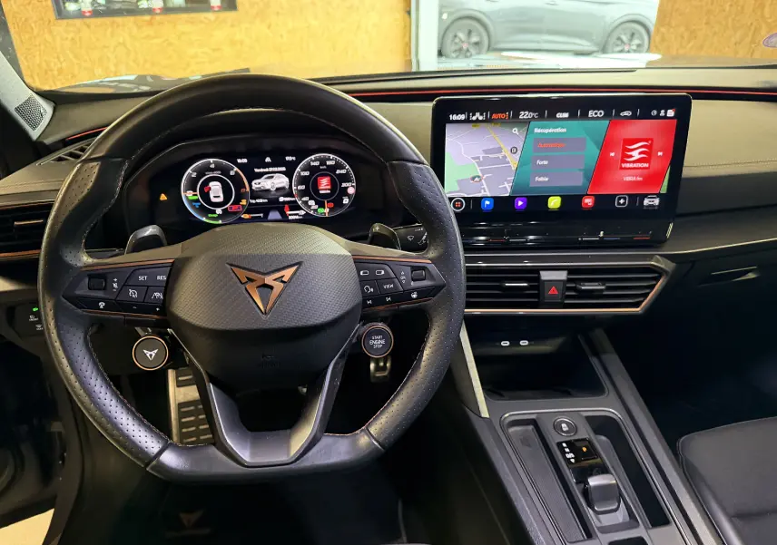 Vue intérieure centrée sur le volant noir perforé et l'écran tactile du tableau de bord du CUPRA Formentor gris 2023.