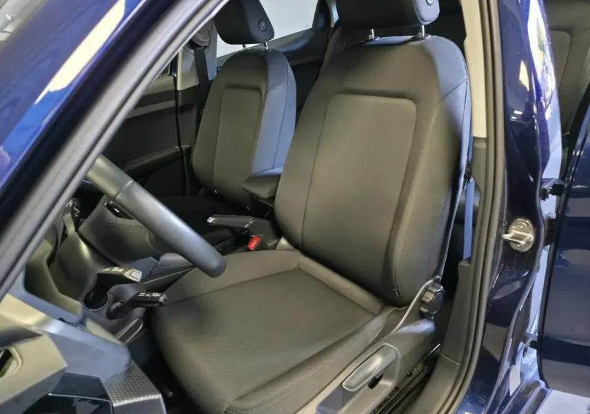 Vue intérieure côté conducteur de l'Audi A1 Sportback 2024 bleu, sièges sport en tissu noir et accoudoir central.