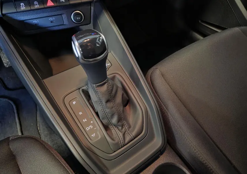 Gros plan sur la console centrale avec levier de vitesses automatique noir et sièges avant en tissu gris dans une Audi A1 Sportback.