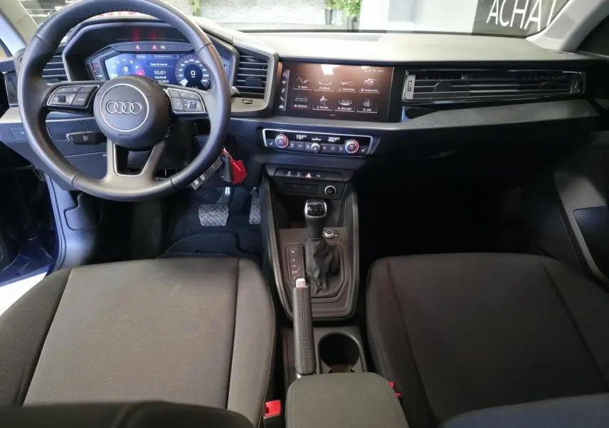 Intérieur Audi A1 Sportback 2024 vu de face, tableau de bord noir avec écran digital et volant cuir multifonctions.